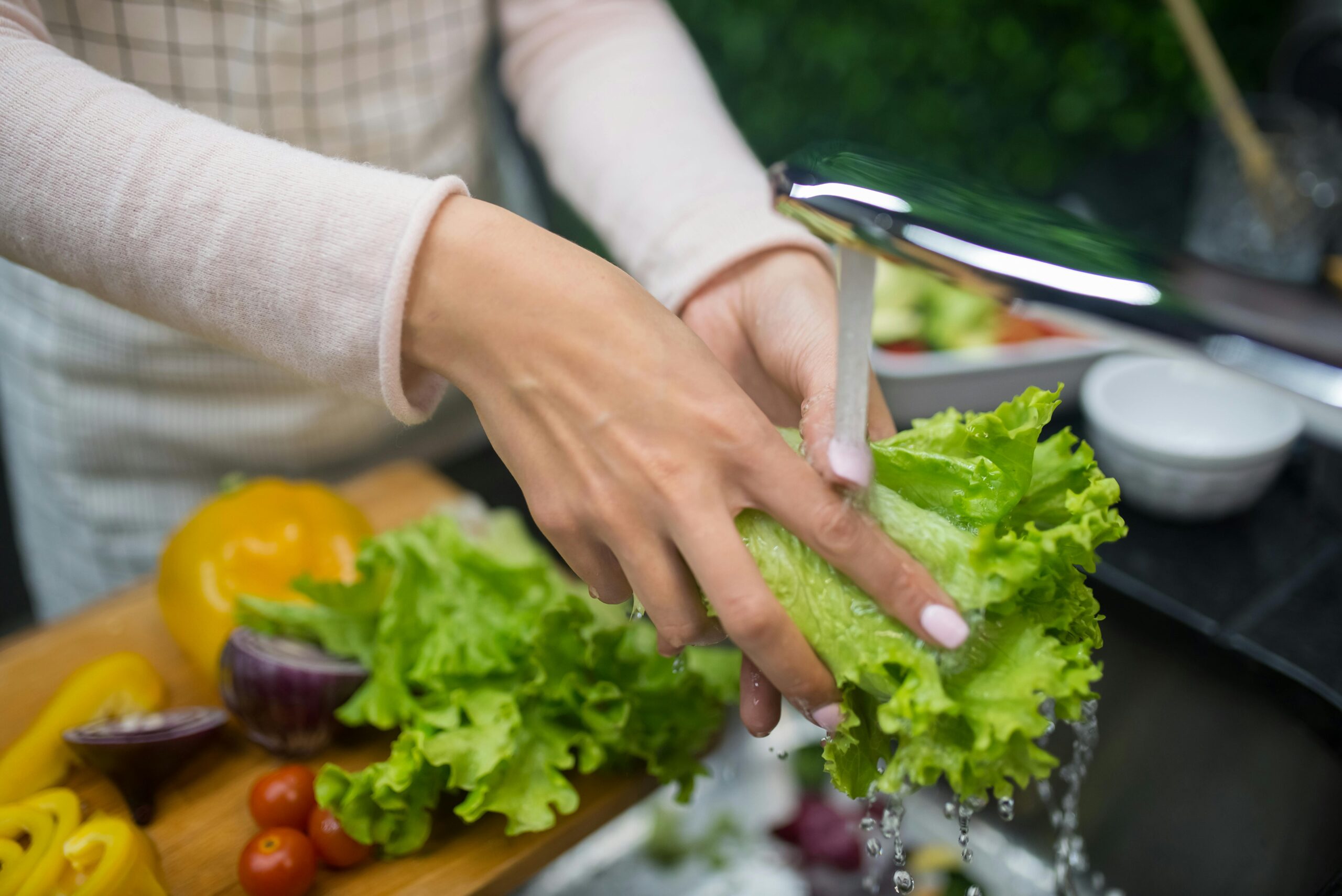 Hands washing fresh lettuce under running water. Healthy food preparation in home kitchen.