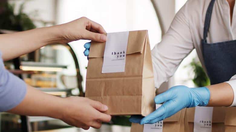 Customer receiving a takeout food bag from a restaurant worker, representing the shift toward reducing single-use utensils under New Jersey’s Skip the Stuff law.